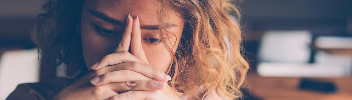 Jonge vrouw leunt met haar hoofd op haar handen die ze gevouwen voor zich houdt