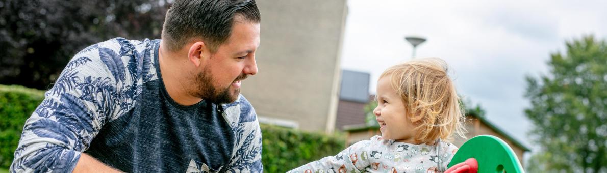 Jonge ouder man met zijn dochtertje in de speeltuin. Dochtertje zit op wipwap.