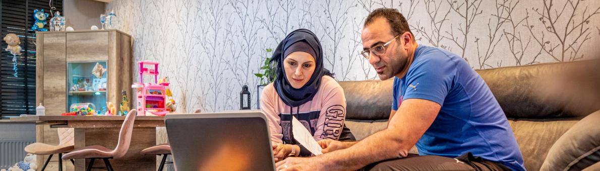 Man en vrouw zitten thuis op de bank. Voor zich hebben zij een laptop en in de hand papieren.