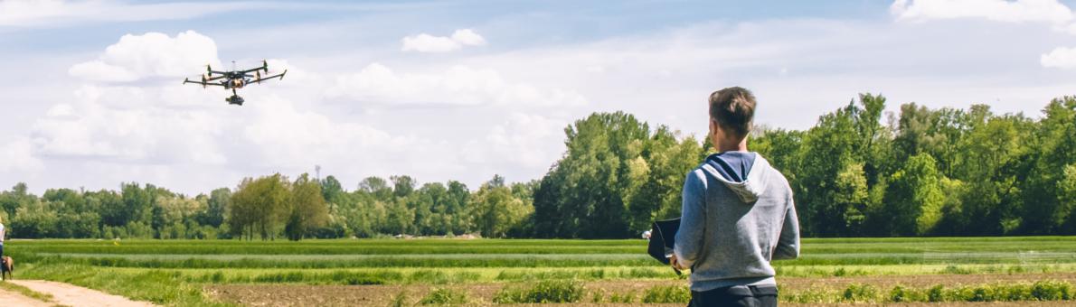 Man staat tussen twee grasvelden in en vliegt met zijn drone