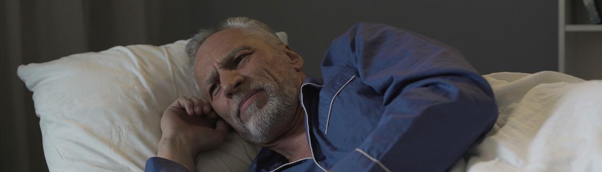Een oudere man ligt wakker in bed. Hij heeft zijn smartphone vast.