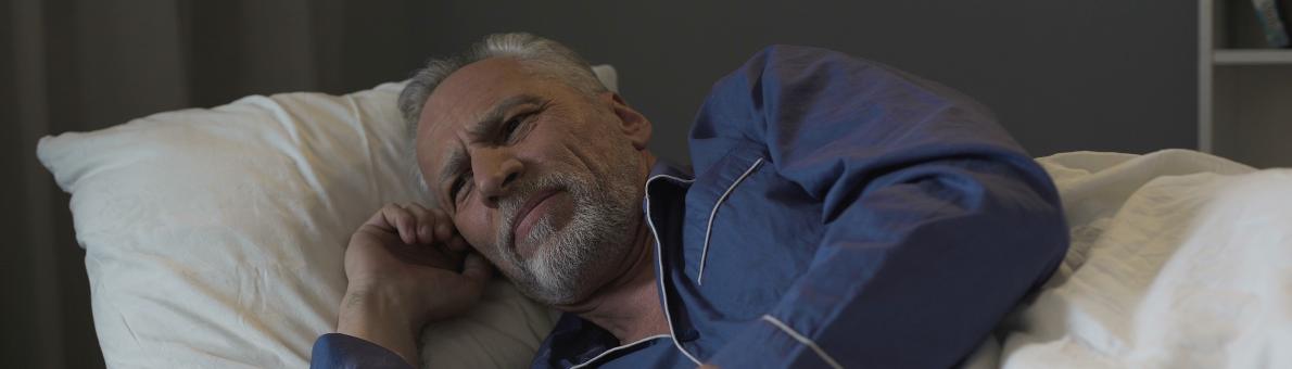 Senior man met grijs haar en grijze baad ligt wakker in bed