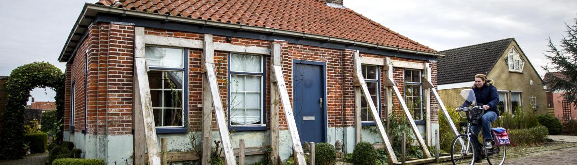 Vrouw op fiets rijdt in Groningen langs huis dat wordt gestut door balken
