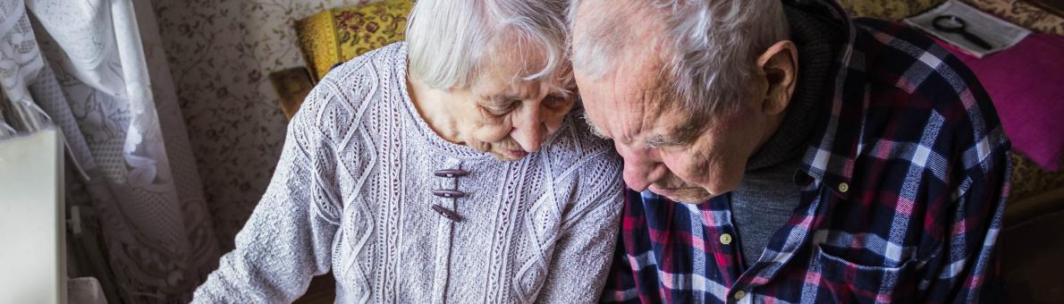 Ouder echtpaar zit naast elkaar bij de verwarming en bekijkt de energierekening