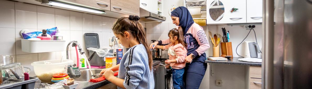 Vrouw met migratieachtergrond staat in de keuken met haar twee kinderen.