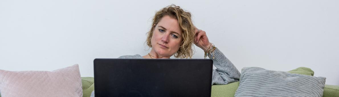 Een vrouw van middelbare leeftijd zit met een laptop op de bank