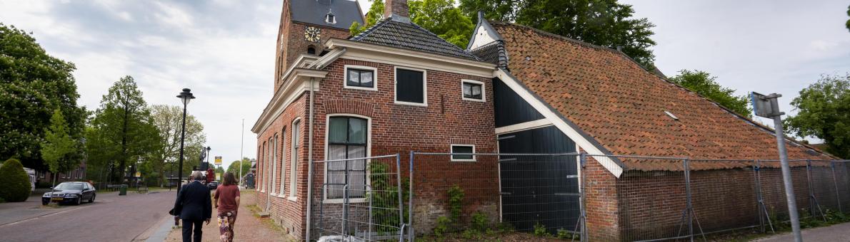 De Nationale ombudsman loopt door een straat in Groningen. Schade van de aardbeving is zichtbaar aan huizen.