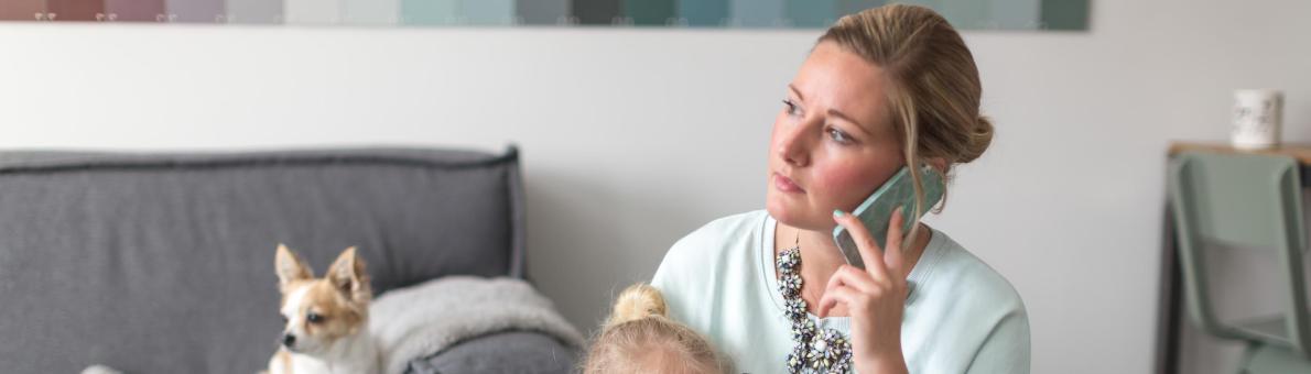 Een vrouw aan de telefoon met kind op schoot