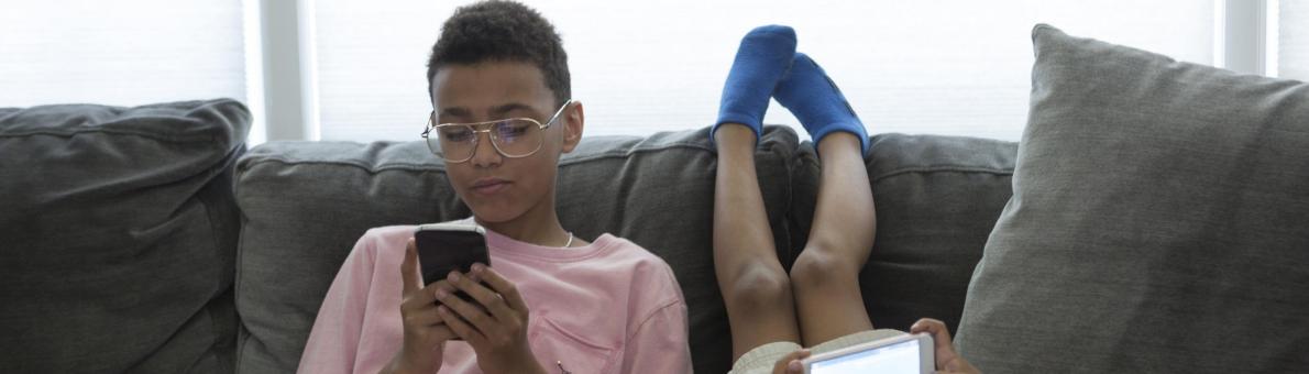 Two kids with phones in their hand laying and sitting on the couch