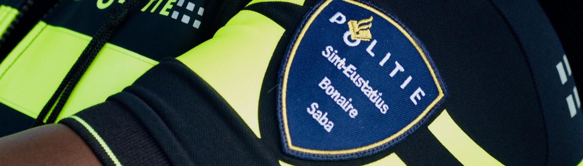 Foto van de mouw van politiekleding met op de mouw gespeld Politie Sint-Estatius, Bonaire en Saba