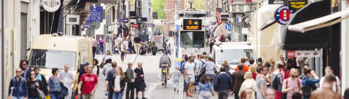 Een foto van een straat in Amsterdam. Je ziet mensen wandelen, tramrails, en aan beide kanten winkels. Een foto van een straat in Amsterdam. Je ziet mensen wandelen, tramrails, en aan beide kanten winkels.