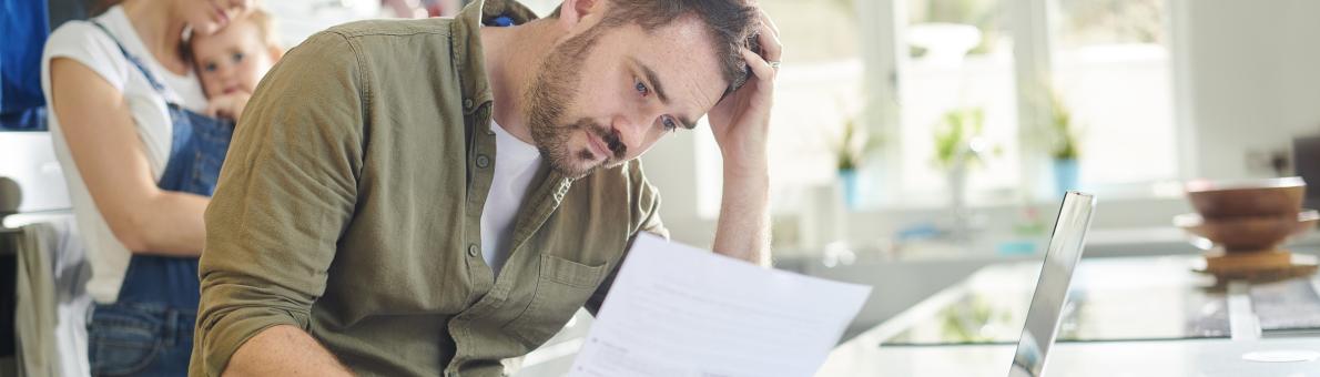 Man, zittend in keuken, kijkt bezorgd naar document in zijn hand