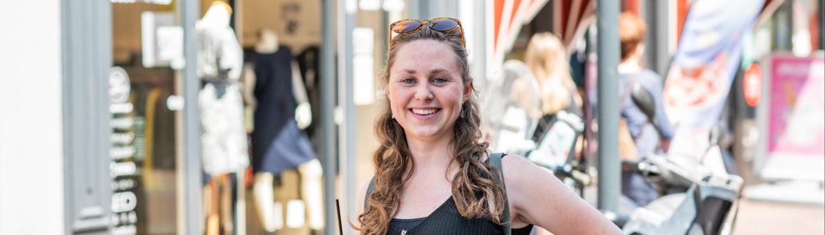 Henrieke, een jongvolwassen vrouw met donkerblond krullend haar staat op straat en heeft een drinkbeker vast.