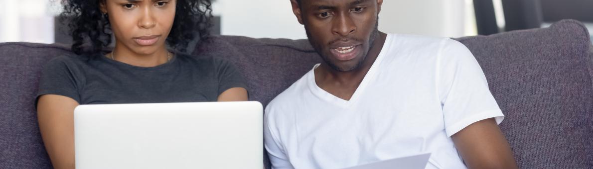 Echtpaar naast elkaar op de bank, kijkt verbaasd naar laptop