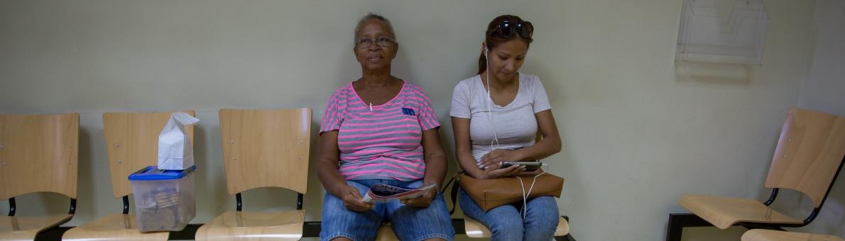 Twee vrouwen zitten op een bankje in de wachtkamer. De foto is genomen op Bonaire.