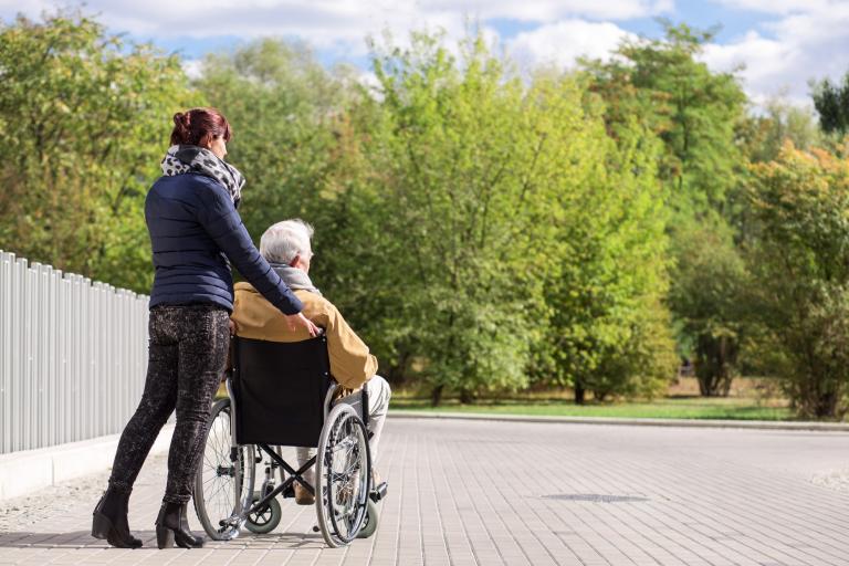 Vrouw in rolstoel maakt samen met vrouw wandeling door park
