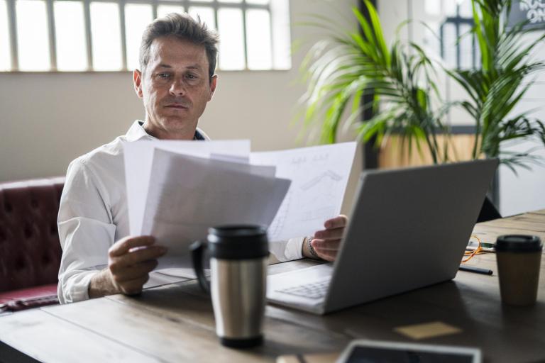 Man neemt papieren door, laptop staat op bureau