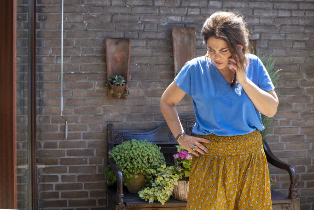 Vrouw staat in de tuin met telefoon aan haar oor