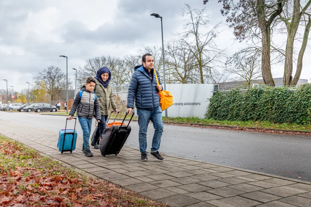 Gezin loopt met koffers bij AZC